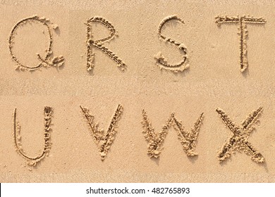 character Q R S T U V W X handwritten on sand.