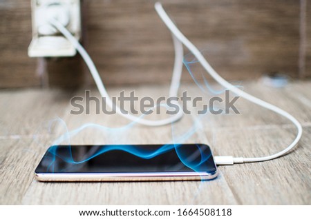 Charching Android Phone battery connected to electricity wire.Overheating Mobile Phone  plugged in to charge all night.Smoke from black screen of cell phone. Overcharging concept