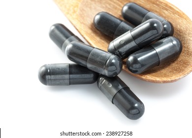 Charcoal capsules on a wooden spoon isolated on white