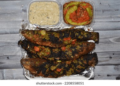 Charcoal Grilled Mullet Fish With Parsley And Tomato, Pickled Eggplant Aubergine And Tahini Sauce, Barbecued And Served In A Disposable Plate On Foil Paper Isolated On Wooden Background