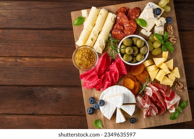 Charcuterie board with a variety of cheeses, salami, chorizzo, prosciutto, honey, grapes, nuts, olives, bread, blueberries and fresh herbs on a dark wooden background. A festive snack