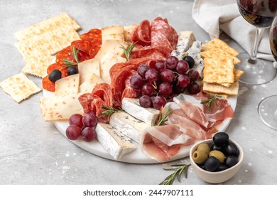 Charcuterie plate with Italian salami and prosciutto ham, with gorgonzrola cheese and pecorino cheese with herbs, served with olives and grapes.   Two glasses of  wine, appetizer platter for aperitif - Powered by Shutterstock