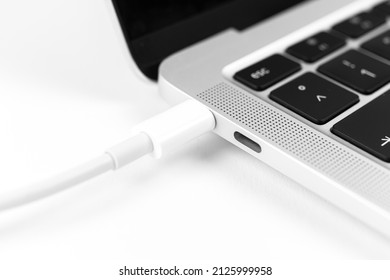 Charging battery laptop. Modern USB C port for fast charge. White cable plugged in laptop close-up view