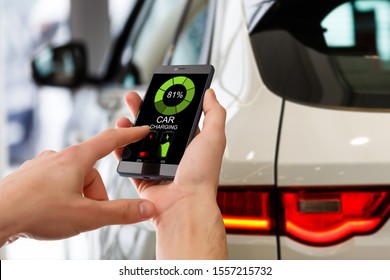 Charging Electric Car Looking At App On Mobile Phone. Close Up Of Smartphone Screen. Hand Holding Smart Device. Mobile Application For Eco Transportation