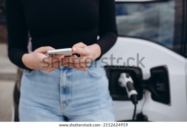 Charging Electric car Looking at App On
Mobile Phone. Close up of smartphone screen. Hand holding smart
device. Mobile application for eco
transportation