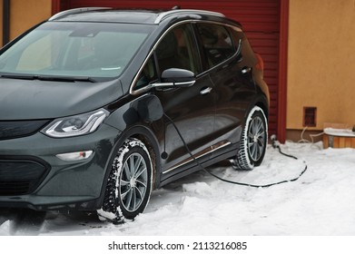 Charging Electric Car In The Yard Of House At Winter.