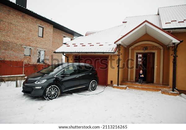 Charging\
electric car in the yard of house at\
winter.