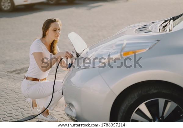 Charging electro car at the electric gas station.\
Woman standing by the\
car.