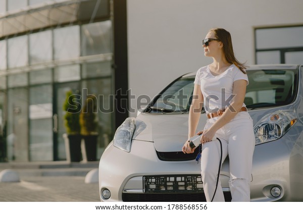 Charging electro car at the electric gas station.
Woman standing by the
car.