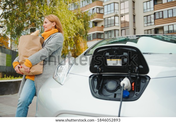 Charging electro car at the electric gas station.\
Woman standing by the\
car.