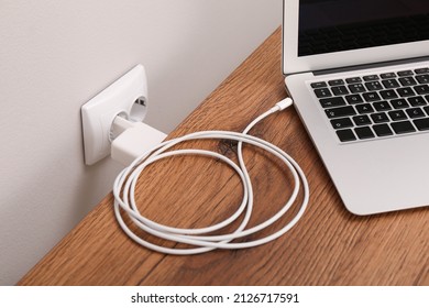 Charging laptop with power adapter in electrical socket on wooden table