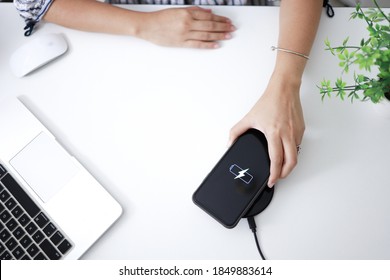 Charging mobile phone battery with wireless charging device in the table. Smartphone charging on a charging pad. Mobile phone near wireless charger