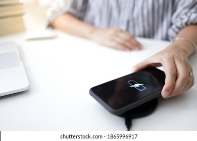 Charging mobile phone battery with wireless charging device in the table. Smartphone charging on a charging pad. Mobile phone near wireless charger