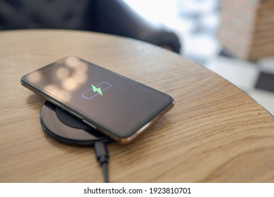 Charging Mobile Phone Battery With Wireless Charging Device In The Table. Smartphone Charging On A Charging Pad. Mobile Phone Near Wireless Charger