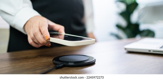 Charging mobile phone battery with wireless charging device in the table. Smartphone charging on a charging pad. Mobile phone near wireless charger Modern lifestyle technology  - Shutterstock ID 2245972273