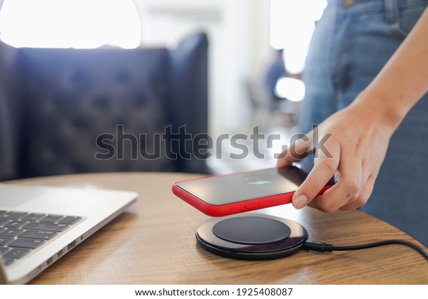 Charging mobile phone battery with wireless
charging device in the table. Smartphone charging on a charging
pad. Mobile phone near wireless
charger