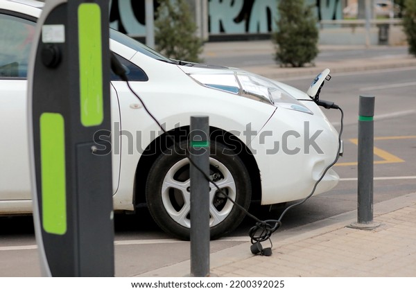 Charging modern\
electric cars, new energy vehicles, NEV, on the street white\
electric car with a cable connected and a charging station.\
Eco-friendly alternative energy concept.\
