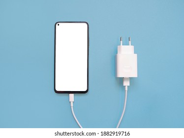 Charging a smartphone via a USB cable on a blue background, top view. Silhouette of a black smartphone with a white blank screen, with a usb charging cable and a power supply on empty space. copy