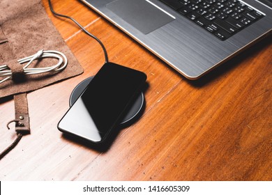 Charging the smartphone with wireless charger on wooden desk.