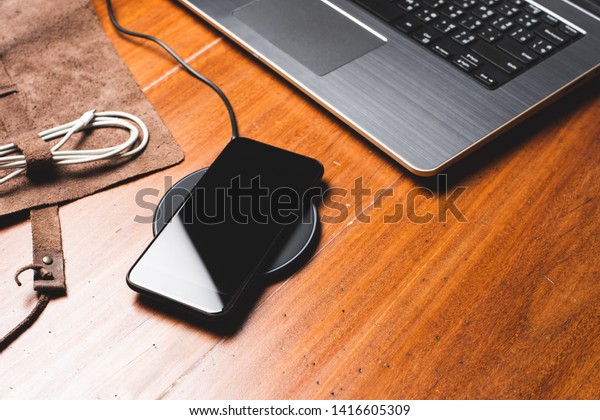 Charging the smartphone with wireless charger on\
wooden desk.