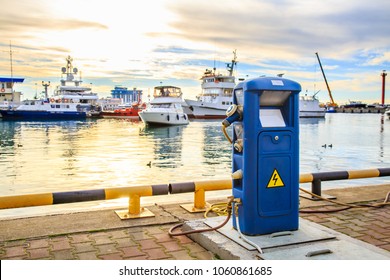 Charging Station For Boats, Electrical Outlets To Charge Ships In Harbor. Shore In Marina Jetty. Electrical Power Sockets Bollard Point On Pier Near Sea Coast. Luxury Yachts Docked In Port At Sunset.