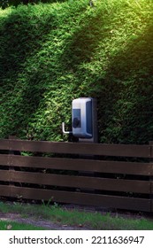 Charging Station For An Electric Car Near A Green Hedge. Thuja And Wooden Fence In The Countryside. The Eco-friendly Way To Fill Up Your Car. Alternative Fuel