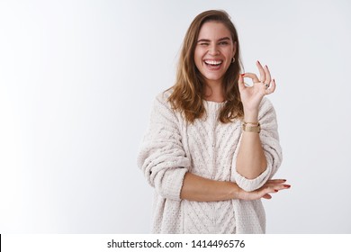 Charismatic confident upbeat gorgeous adult woman wearing loose stylish sweater cozy, winking flirty sassy smiling broadly showing okay ok gesture excellent mood, assuring everything awesome
