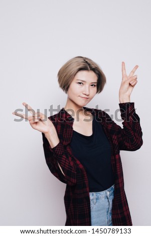 charismatic and creative girl with short hair posing near the white wall. emotional portrait of a student actress. street style clothing: plaid men's shirt. women are actively gesticulating hands