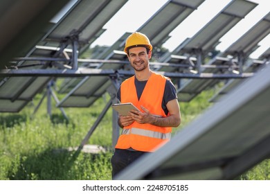 Charismatic with a cute smile young technician at solar power farm he holding his tablet to continue to work he standing in the middle of photovoltaic solar rows - Powered by Shutterstock