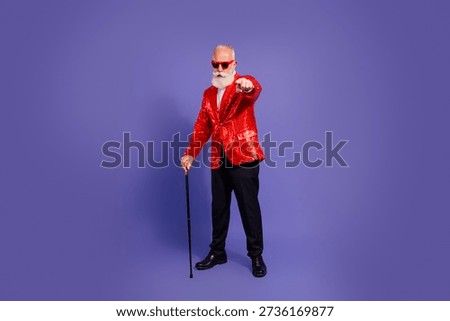 A charismatic elderly man with a white beard wears a bright red sequin jacket and black pants. He points at the camera, creating a lively festive mood against a purple background.
