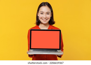 Charismatic Fun Young Woman Of Asian Ethnicity 20s Years Old Wears Orange Shirt Hold Use Work On Laptop Pc Computer With Blank Screen Workspace Area Isolated On Plain Yellow Background Studio Portrait