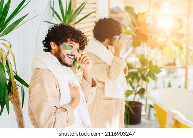 Charismatic Hispanic Man In Beige Bathrobe Enjoy Morning Routine In Cozy Bathroom Interior With Mirror And Green Plants. Cosmetology Beauty And Lifestyle Concept