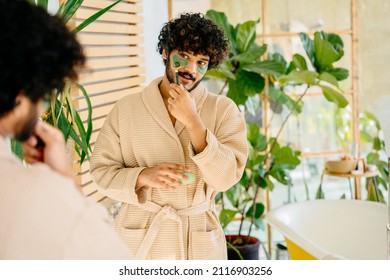 Charismatic Hispanic Man In Beige Bathrobe Enjoy Morning Routine In Cozy Bathroom Interior With Mirror And Green Plants. Cosmetology Beauty And Lifestyle Concept