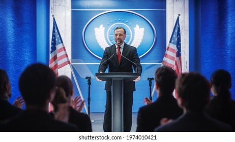 Charismatic Organization Representative Speaking At A Press Conference In Government Building. Press Officer Delivering A Speech At A Summit. Minister At Congress. Backdrop With American Flags.