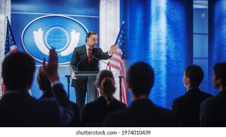 Charismatic Organization Representative Speaking At A Press Conference In Government Building. Press Officer Delivering A Speech At A Summit. Minister At Congress. Backdrop With American Flags.