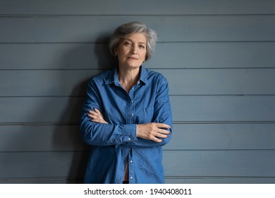 Charismatic Person. Serious Elderly Latin Lady Posing For Portrait Keep Arms Crossed. Confident Old Female Mother Grandma In Stylish Jeans Jacket Stand By Grey Planked Wall Look At Camera. Copy Space