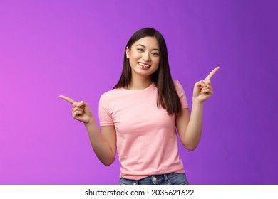 Charismatic relaxed cute asian woman short haircut pointing sideways introduce variety choices, showing left and right products, smiling joyfully, easily making decision, stand purple background