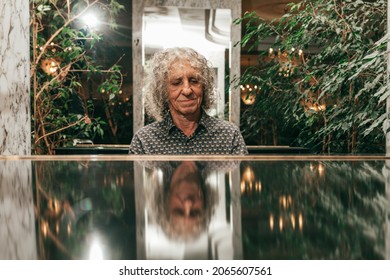 charismatic senior man with curly gray hair is playing piano in lobby of hotel, enjoying his hobby. Active senior
