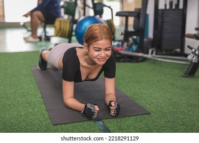 A charismatic woman smiles while doing planks on a black mat. Having fun and a lighthearted moment at the gym. - Shutterstock ID 2218291129