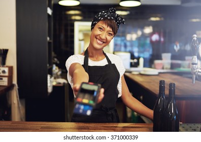 Charismatic young female small business owner requesting payment form a client holding out a handheld banking machine to process their credit card, focus to her face and warm friendly smile - Powered by Shutterstock