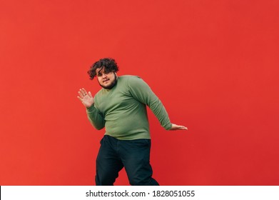 Charismatic Young Man With Curly Hair And Overweight Dancing Hip Hop On The Street On A Red Background. The Fat Man Shows A Dance Performance, Isolated.