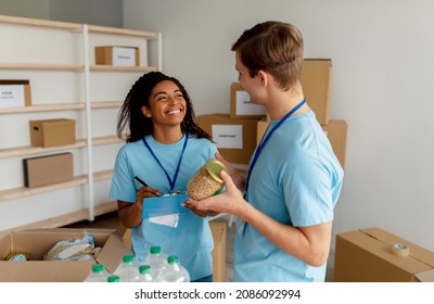 Charity Center Work. Happy Female Manager Checking Donation List And Writing In Clipboard, Talking With Volunteer While Working In Charity Organization And Packing Donations Boxes