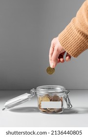 Charity, Donation And Saving Concept - Close Up Of Female Hand Putting Coin Into Glass Jar