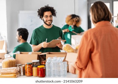 charity, donation and volunteering concept - happy smiling male volunteer with clipboard and woman taking box of food at distribution or refugee assistance center - Powered by Shutterstock