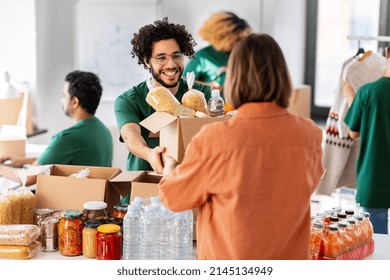 charity, donation and volunteering concept - happy smiling male volunteer giving box of food to woman at distribution center at distribution or refugee assistance center - Powered by Shutterstock