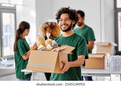 charity, donation and volunteering concept - happy smiling male volunteer with food in box and international group of people at distribution or refugee assistance center