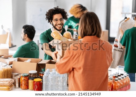 charity, donation and volunteering concept - happy smiling male volunteer giving box of food to woman at distribution center at distribution or refugee assistance center