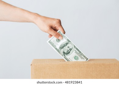 Charity, Finances, Funding, Investment And People Concept - Male Hand Putting Dollar Money Into Donation Box