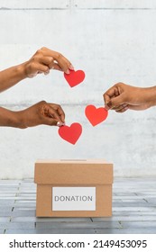 charity, love and valentine's day concept - close up of hands putting red hearts into donation box over urban steet background