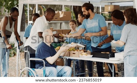 Charity organization shows devotion to fighting hunger and poverty by giving away free meals to homeless people. Warm food is provided by volunteers to caucasian wheelchair user and less privileged.